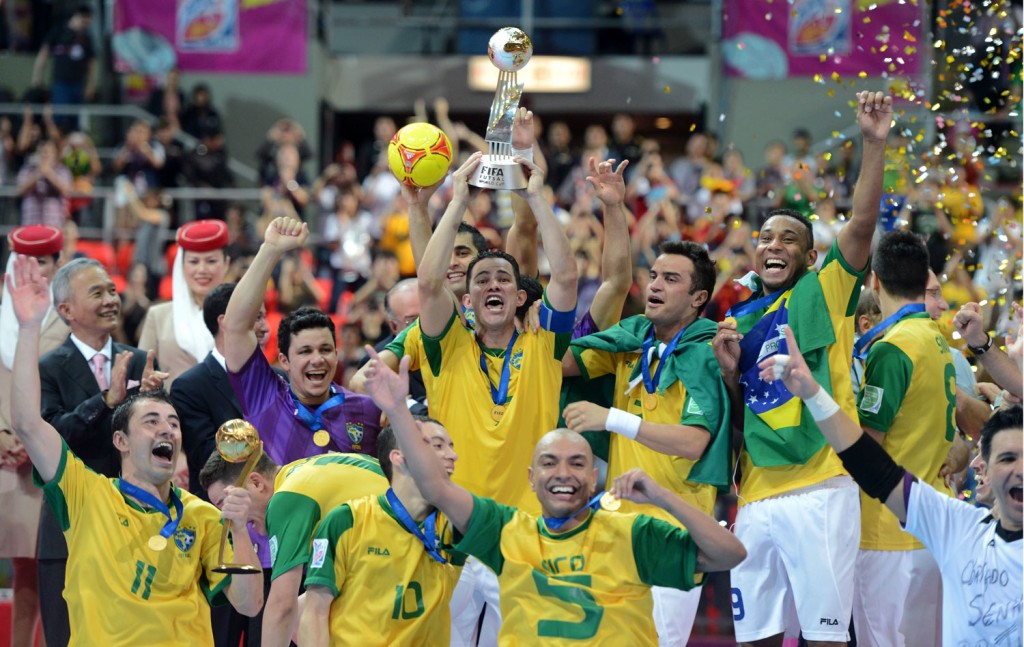 Vinicius ergue a taça do mundial de 2012, e Falcão comemora. Os dois esperam ver Bateria comemorando tal título